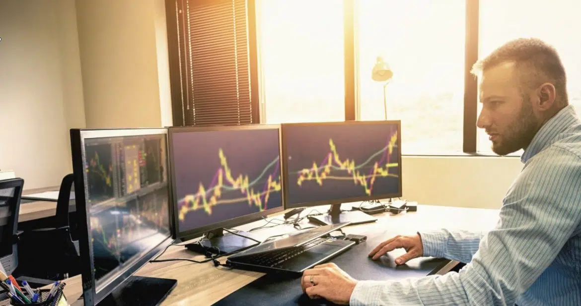 Homme devant trois écrans avec la bourse