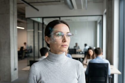 Femme portant des lunettes de réalité augmentée intelligentes dans un bureau moderne, interface holographique visible à travers les verres