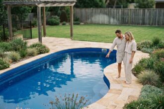 Couple examinant une piscine coque en polyester installée dans un jardin résidentiel avec dallage en pierre naturelle